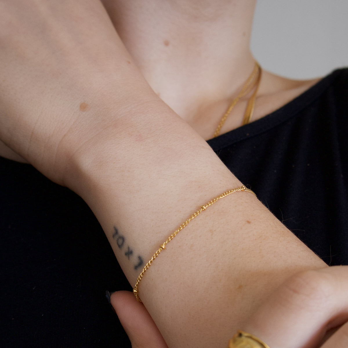 Close-up of a person's wrist with gold bracelet with tiny gold beads on a neutral background