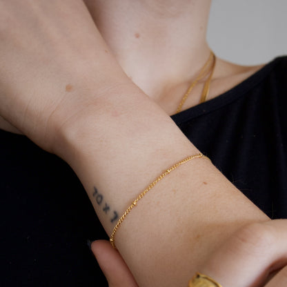 Close-up of a person's wrist with gold bracelet with tiny gold beads on a neutral background